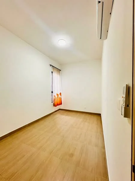 Room features: light wood laminate flooring, white painted walls, single ceiling light fixture, wall-mounted air conditioning unit, curtains with orange pattern, no visible furniture, empty room; style: minimalist.