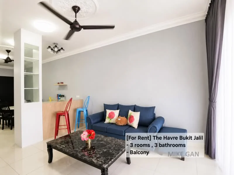 Living features: 3-seater fabric sofa in blue, coffee table with black marble top, ceiling fan with 3 blades, recessed downlights, grey painted walls, white ceiling with decorative plaster, large window with grey curtains, open layout to kitchen area, decorative cushions on sofa, tile flooring; style: modern. Kitchen features: bar counter with wooden finish, stools at counter, open shelving, white cabinets, kitchen appliances visible; style: modern. Room features: balcony access, grey walls, floor-to-ceiling windows.