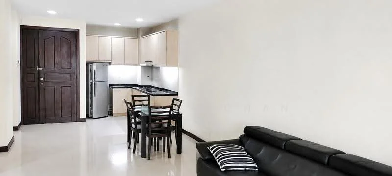 Living features: black leather sofa, white walls, glossy tile flooring, recessed downlights, decorative throw pillow, dining table with four chairs, kitchen area with cabinets, stainless-steel fridge, black countertop, kitchen cabinets with wood finish; style: modern.