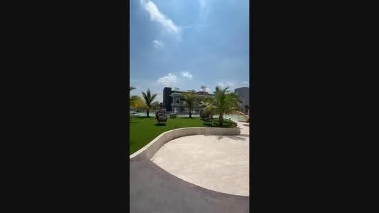 Exterior features: manicured lawn, palm trees, landscape garden, swimming pool visible in background, stone-paved walkway, modern architectural design, outdoor seating area, water feature, sunny weather, clear blue sky; style: modern.