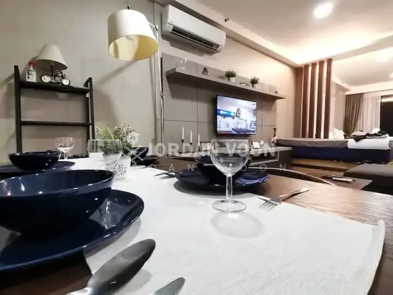 Living features: wall-mounted TV, sofa with cushions, dining table with tablecloth, blue dinner plates, wine glasses, cutlery, shelf with decorative items, air conditioning unit, recessed lighting, wooden flooring, grey accent wall, curtains, bed in background; style: modern.