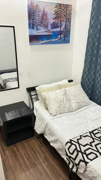 Bedroom features: queen-size bed, white bedding, decorative pillows, black bedside table, mirror, framed artwork on wall, blue curtains, wooden flooring; style: modern.