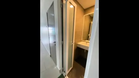 Bathroom features: glass shower enclosure, single-sink vanity with white cabinet, mirror above vanity, tile flooring, neutral wall tiles, recessed lighting, towel rack, dark mat on floor; style: modern.