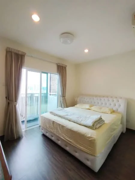 Bedroom features: queen-size bed with upholstered headboard, light yellow bedding, wooden flooring, white painted walls, curtains in beige, sliding glass door, balcony access, ceiling light fixture, air conditioning unit; style: modern.