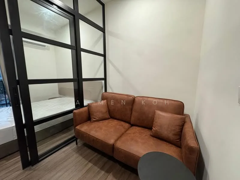Room features: brown leather sofa with two cushions, small round side table, glass partition wall, light wood flooring, white painted walls, wall-mounted air conditioning unit, bed visible through glass partition; style: modern.