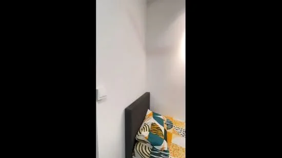 Bedroom features: white painted walls, grey headboard, colorful bedding with geometric patterns, decorative pillows, wall-mounted light switch.