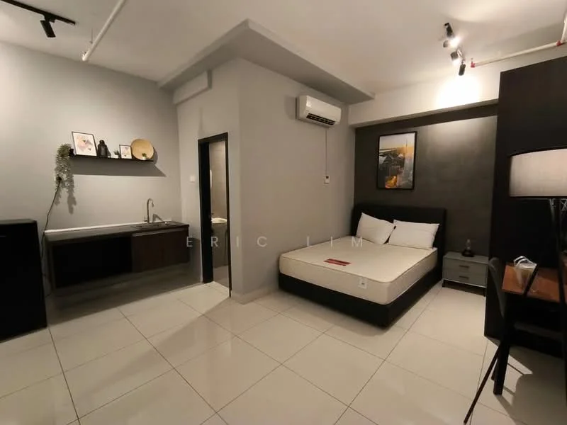 Room features: white painted walls, grey accent wall, tile flooring, queen-size bed, upholstered headboard, nightstand, table lamp, wall-mounted air conditioning unit, kitchenette with sink, dark wood cabinetry, refrigerator, small dining table, decorative artwork, recessed lighting; style: modern.