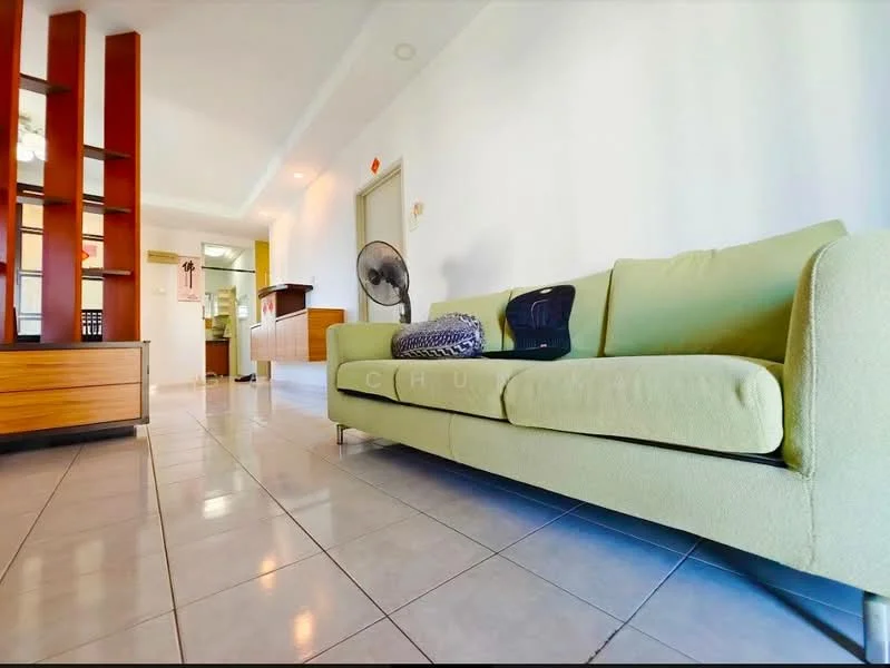 Living features: green fabric sofa, ceramic tile flooring, wall-mounted fan, wooden shelving unit, neutral wall colour, open layout, natural light from windows, decorative throw pillows; style: modern. Room features: kitchen area visible in background, doorway leading to other rooms.