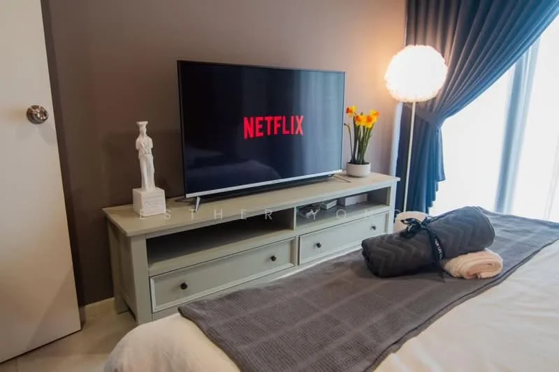 Bedroom features: queen-size bed, white bedding, grey throw blanket, decorative pillows, TV console with drawers, wall-mounted TV, statue decoration, table lamp with round shade, curtains, floor-to-ceiling windows, light-colored flooring, accent wall in dark color; style: modern.