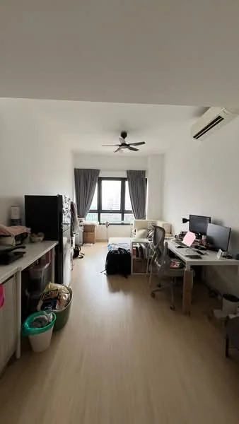 Living features: white painted walls, light wood flooring, 5-blade ceiling fan, floor-to-ceiling window, grey curtains, desk with computer monitors, office chair, kitchenette with fridge, kitchen counter, storage bins, laundry basket, backpack; style: modern; view: city.