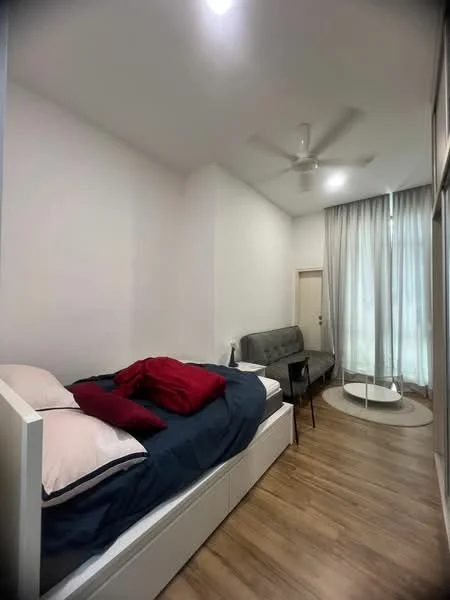 Bedroom features: single bed with white frame, blue bedding with red throw pillows, wooden flooring, ceiling fan, large window with sheer curtains, grey sofa, round coffee table, white walls; style: modern.