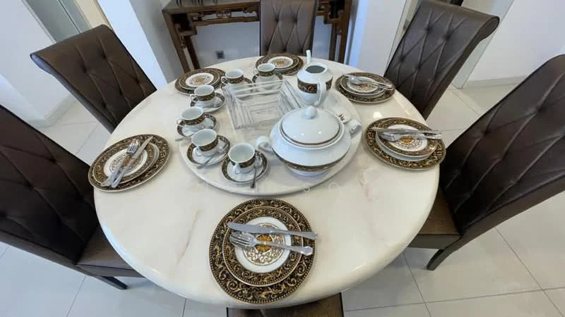 Dining features: round marble dining table, 8 dining chairs with brown leather upholstery, decorative dinnerware set with gold accents, teapot and cups on the table, silver cutlery, white porcelain plates, glass centerpiece, white tiled flooring; style: modern.