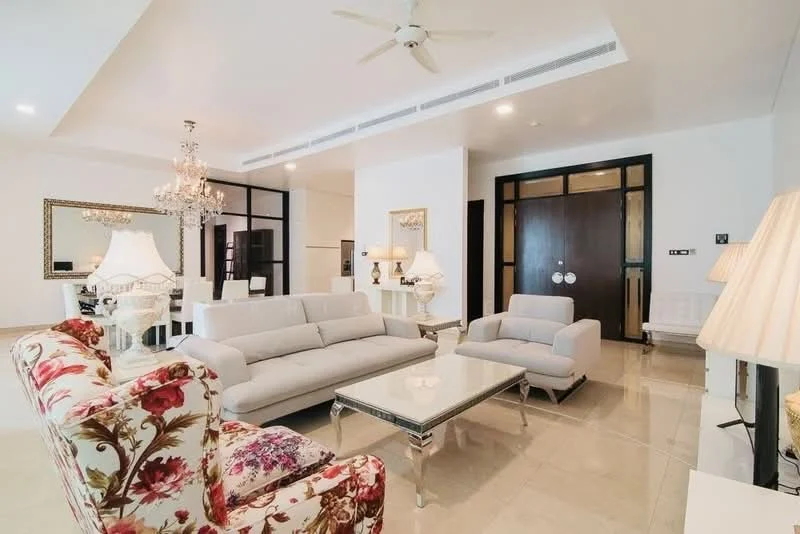 Living features: 3-seater fabric sofa in light grey, 2-seater fabric sofa in light grey, floral upholstered armchair, glass coffee table with metallic base, chandelier with multiple bulbs, recessed downlights, ceiling fan, marble tile flooring, white painted walls, decorative mirror, wall-mounted artwork, side table with lamp; style: modern.