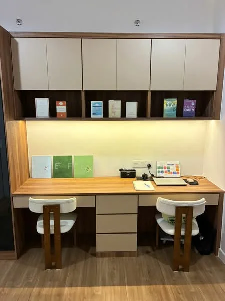 Study features: built-in wooden desk, two white swivel chairs, light wood flooring, cream cabinetry, open shelving above desk, under-cabinet LED lighting, decorative books and materials on shelves, power outlet on desk; style: modern.
