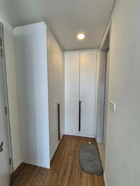 Room features: white painted walls, wood laminate flooring, built-in cabinets with wooden handles, recessed ceiling lights, door with silver handle, grey mat on the floor; style: modern.