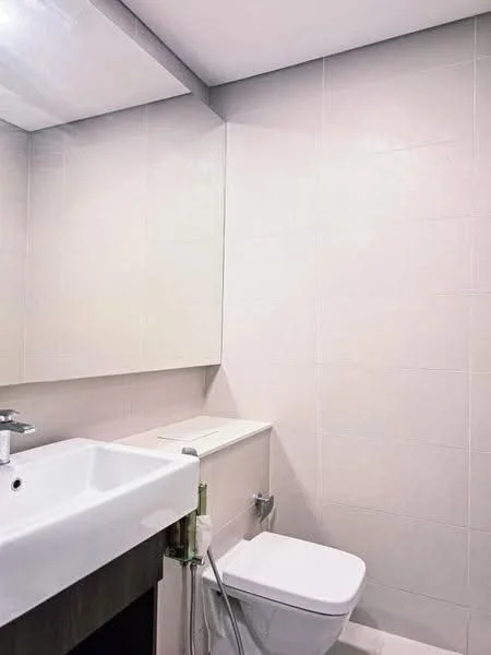 Bathroom features: single-sink vanity with white cabinet, chrome basin mixer faucet, framed mirror, white tiled walls, light grey tiled flooring, one-piece toilet, toilet paper holder, wall-mounted storage shelf; style: modern.