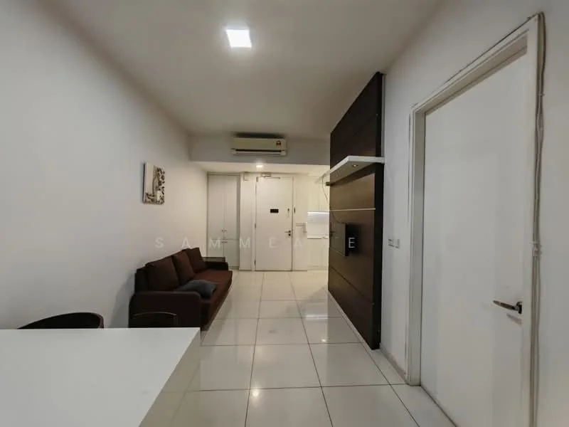 Living features: white painted walls, glossy tile flooring, 1 wall-mounted split AC, 3-seater fabric sofa in brown, recessed LED downlights, wall-mounted TV console, door leading to hallway, decorative artwork on wall; style: modern.