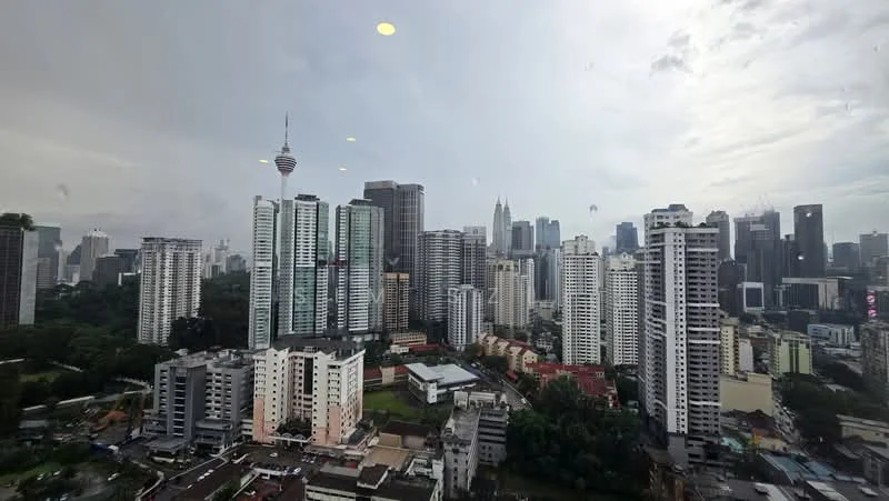 Exterior type: high-rise condominium; features: city skyline view, glass curtain wall, surrounded by mature greenery, urban context, multiple high-rise buildings, visible telecommunications tower; style: modern.