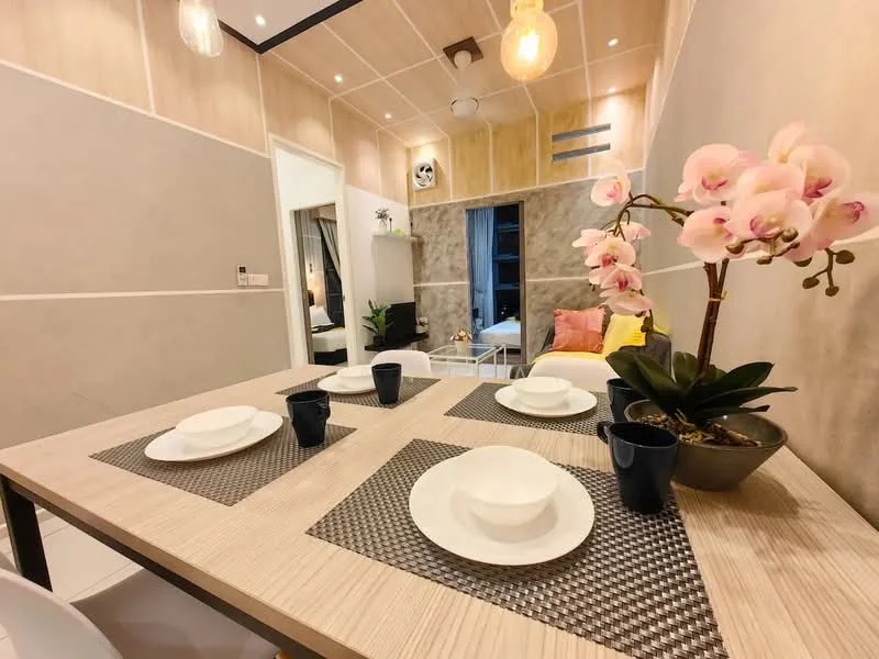 Dining features: wooden dining table, 4 white dining plates, 4 black cups, woven placemat, decorative orchid plant, grey accent wall, light wood paneling, recessed ceiling lights, floor-to-ceiling window, sofa in background, textiles in pink and yellow; style: modern. Living features: sofa, decorative cushions, TV console, wall-mounted TV; style: modern.