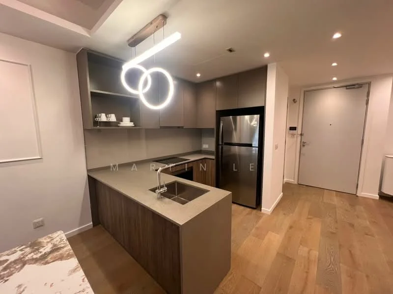 Kitchen features: kitchen island with countertop, single-bowl stainless-steel sink, chrome pull-down faucet, stainless-steel fridge, flat-panel cabinetry in grey, wood cabinetry, recessed downlights, pendant light fixture, wooden flooring, open layout, wall-mounted cabinets, countertop with stone finish; style: modern.