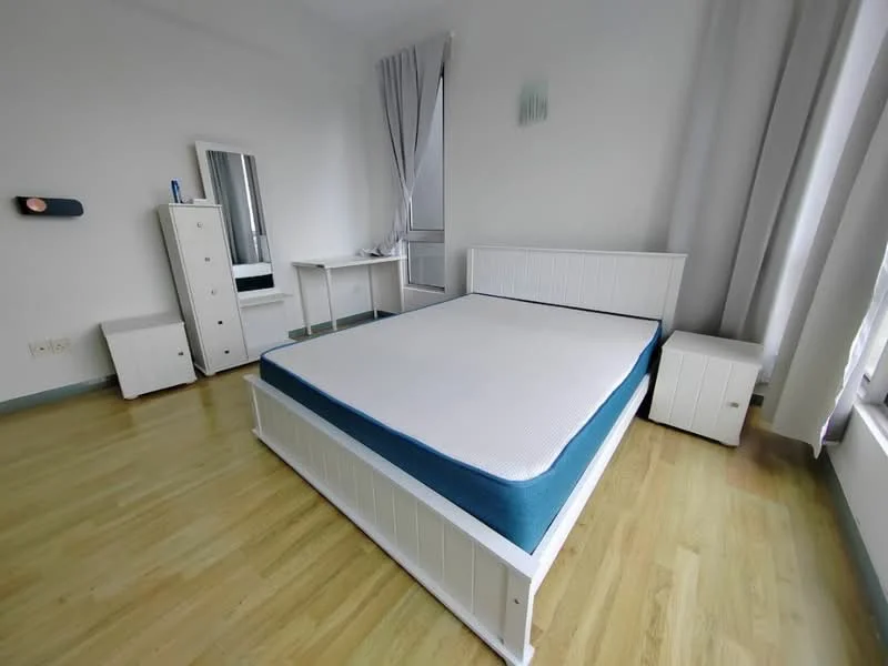 Bedroom features: queen-size bed with white wooden frame, mattress with blue border, white bedside tables, white chest of drawers, full-length mirror, curtains in light grey, wooden flooring, desk with chair; style: modern.