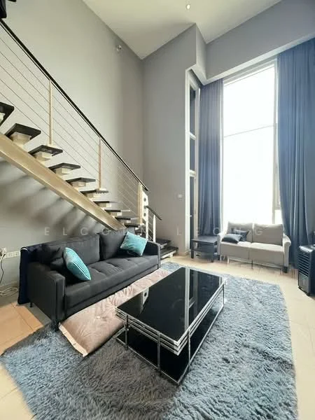 Living features: grey painted walls, high ceiling, large floor-to-ceiling windows, black fabric sofa, blue accent cushions, glass coffee table, area rug in light blue, wooden staircase with metal railing, seating area with two chairs, curtains in dark grey; style: modern.