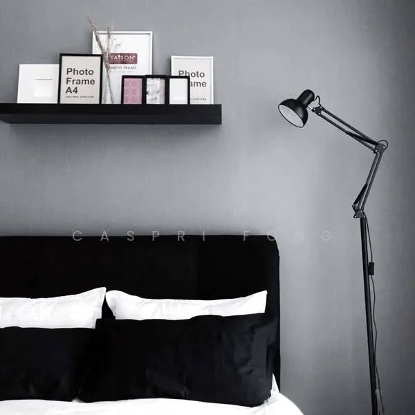 Bedroom features: black upholstered headboard, black bedding with white pillows, grey painted walls, black floor lamp, floating shelf, framed artwork on shelf, decorative photo frames, minimalist decor; style: modern.