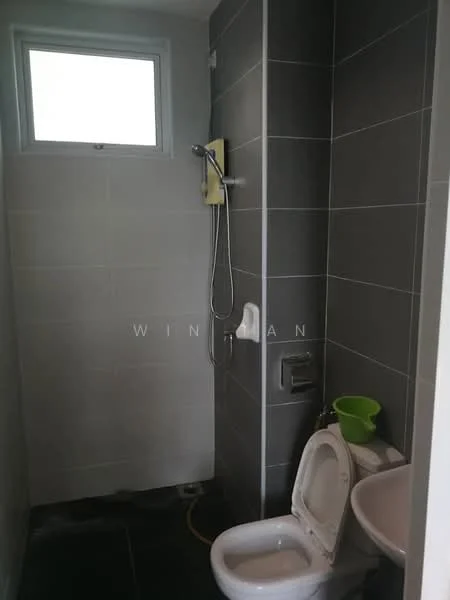 Bathroom features: grey tiled walls, white ceramic toilet, chrome shower head, wall-mounted shower faucet, small sink with chrome faucet, window for natural light, black tiled flooring, green plastic bucket; style: modern.