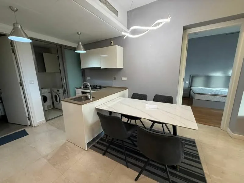 Kitchen features: white cabinetry, marble countertop, stainless-steel sink, chrome pull-down faucet, built-in oven, 4-burner gas hob, refrigerator, washer-dryer combo, pendant lighting; style: modern. Dining features: 6-seater dining table, upholstered dining chairs, area rug with geometric pattern, pendant light fixture; style: modern. Room features: light grey painted walls, tile flooring, floor-to-ceiling windows.