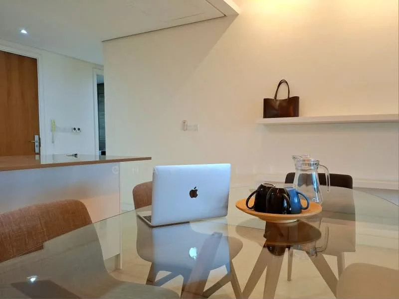 Dining features: glass dining table, 4 upholstered dining chairs, wooden serving tray, black teapot, glass water pitcher, laptop on table, white painted walls, recessed downlights, shelf on wall, brown leather handbag, open kitchen view; style: modern.