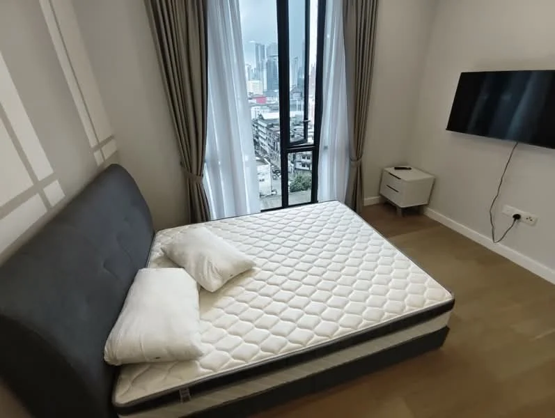 Bedroom features: queen-size bed, grey upholstered headboard, two white pillows, floor-to-ceiling window, curtains, wall-mounted TV, light wood flooring, white bedside table; style: modern; view: city.