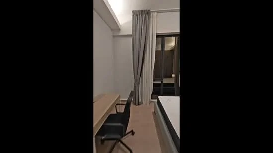 Bedroom features: white painted walls, light wood flooring, floor-to-ceiling windows, sheer curtains, desk with wooden surface, black office chair, queen-size bed, bedding visible, decorative wall light, built-in wardrobe; style: modern.