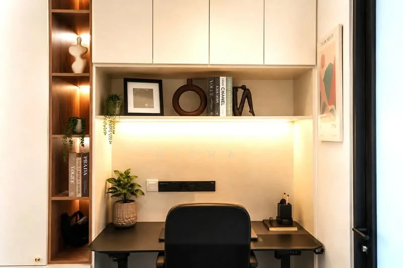Study features: built-in desk with black surface, white cabinetry above desk, wooden shelving with decorative items, framed artwork on wall, greenery in ceramic pot, LED strip lighting under shelves, black office chair, power outlet on wall; style: modern.