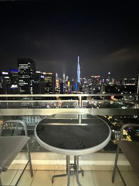 Balcony features: glass railing, round glass-top table, 2 metal chairs, city skyline view, night lighting; style: modern; view: city.