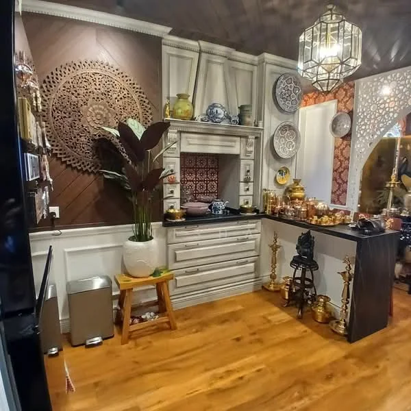 Room features: wooden flooring, decorative wall paneling, intricate wall decor, built-in cabinetry, black countertop, decorative vases, ornamental figurines, hanging pendant light, potted plant, wall-mounted shelves, ceramic dishware, textured wall with geometric pattern, stool, waste bin; style: traditional.