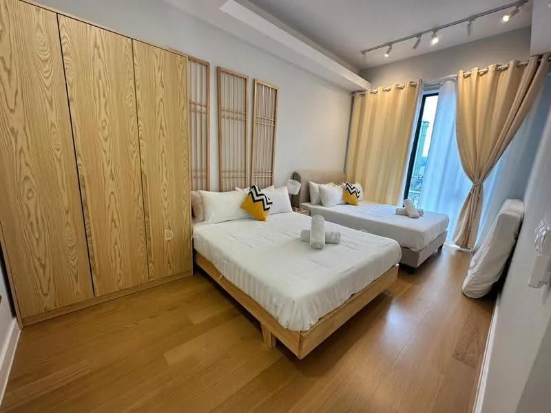 Bedroom features: two single beds with white bedding, wooden bed frames, decorative yellow and black cushions, built-in wooden wardrobe with sliding doors, floor-to-ceiling window, sheer curtains, wooden flooring, recessed ceiling lights; style: modern; view: city.