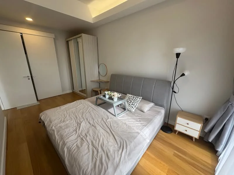 Bedroom features: queen-size bed with grey upholstered headboard, light wood flooring, white painted walls, recessed ceiling lights, floor-to-ceiling wardrobe with sliding doors, small bedside table with drawer, decorative tray on bed, table lamp, decorative cushion, wall-mounted lamp; style: modern.