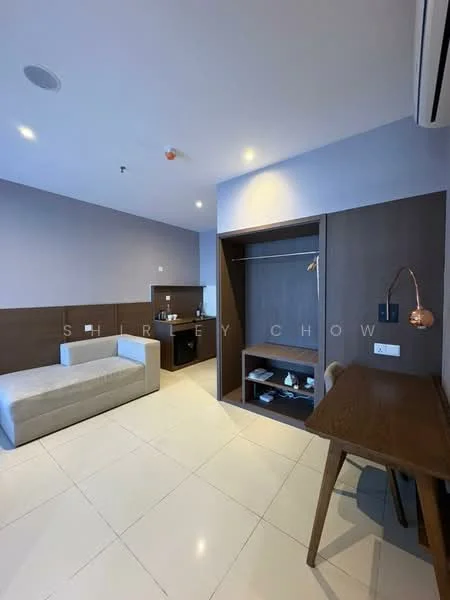 Room features: light grey fabric sofa, white wall, brown accent wall, white tiled flooring, built-in wardrobe with open shelving, wooden desk with copper lamp, mini fridge, wall-mounted air conditioning unit, recessed ceiling lights; style: modern.