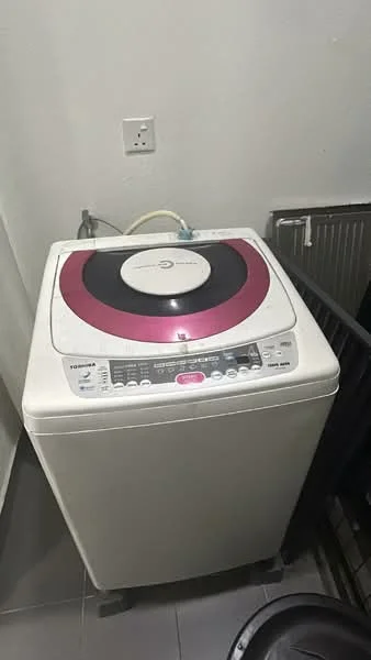 Laundry features: top-load washing machine, white appliance, pink accent on lid, control panel with buttons, drain hose, grey tiled flooring, wall-mounted utility shelf.