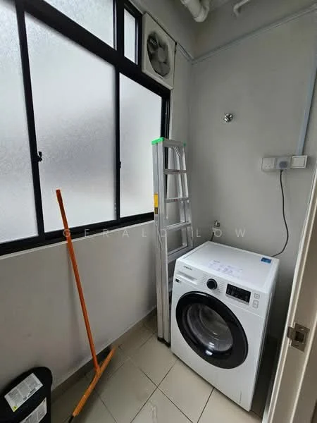 Laundry features: front-load washing machine, tiled flooring, grey painted walls, large window with frosted glass, ladder, broom, wall-mounted fan, storage bin.