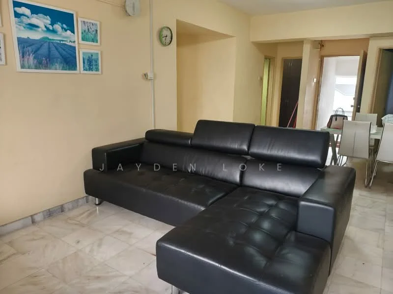 Living features: black leather sectional sofa, marble flooring, cream painted walls, wall clock, framed artwork on walls, open layout to dining area, natural light from adjacent room; style: modern.