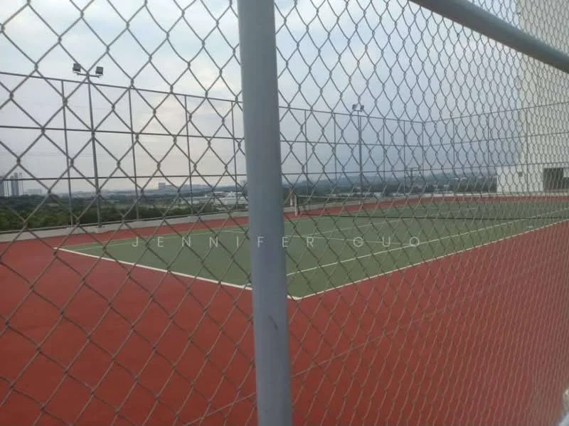 Exterior type: tennis court; features: fenced tennis court, red synthetic surface, green playing area, floodlights for night play, surrounding greenery, view of city skyline; style: modern.