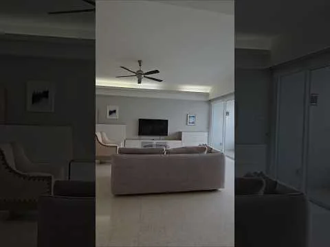 Living features: 5-blade ceiling fan with light, wall-mounted TV, sofa in light fabric, armchairs in light fabric, coffee table, recessed downlights, sliding glass door, floor-to-ceiling windows, light-coloured walls, marble flooring; style: modern; view: garden.