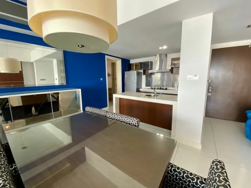 Dining features: glass dining table, upholstered dining chairs with black and white pattern, blue accent wall, mirrored wall, white ceiling, recessed downlights, floor tiles, open layout to kitchen; style: modern. Kitchen features: stainless-steel appliances, built-in oven, gas hob, stainless-steel range hood, dark wood cabinetry, white countertop, open shelving, kitchen island; style: modern.