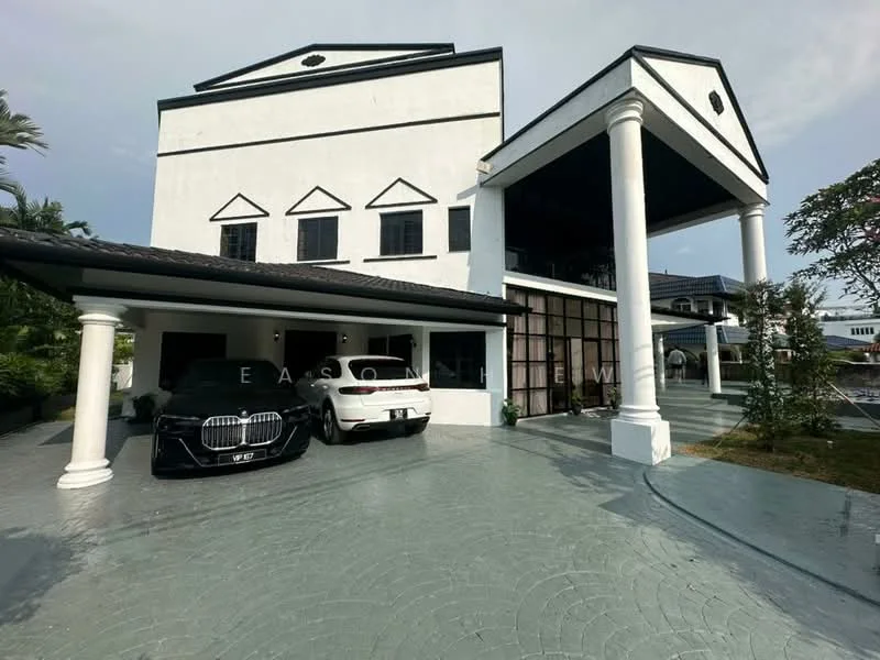 Exterior type: detached bungalow; features: white painted facade, flat roof, 2-storey building, large glass windows, columns at entrance, paved driveway, manicured landscaping, two parked cars, outdoor steps leading to entrance, surrounded by greenery; style: modern.