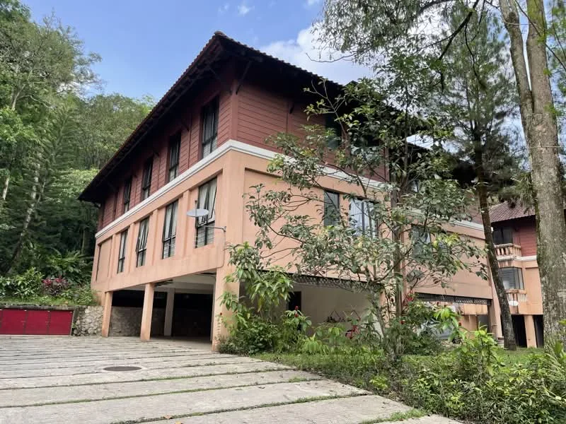 Exterior type: detached bungalow; features: two-storey building, pink painted facade, wooden accents, large windows, exposed stone base, landscaped garden, manicured lawn, driveway with interlocking pavers, surrounded by greenery, balcony on upper floor, air conditioning unit visible; style: traditional.