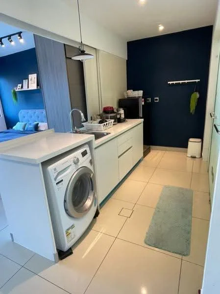 Laundry features: white washing machine, single-bowl stainless-steel sink, chrome pull-down faucet, white cabinetry, grey countertop, blue accent wall, recessed downlights, pendant light, tile flooring, small white stool, greenery wall decor, open shelving; style: modern.