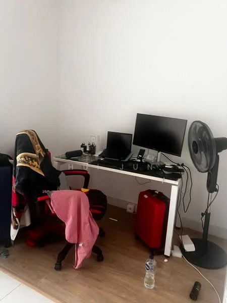 Study features: white painted walls, wooden flooring, desk with dual monitors, red office chair, standing fan, red suitcase, water bottle, clothing draped over chair.