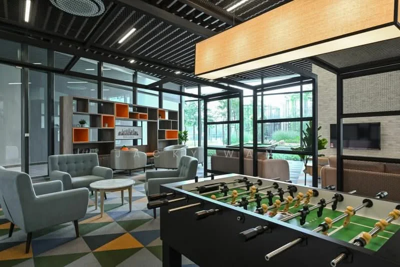 Room features: glass walls, black metal framing, green and grey patterned carpet, sofa in light grey, sofa in teal, wooden coffee table, foosball table, suspended rectangular light fixture, built-in shelving with orange and white accents, wall-mounted TV, indoor plants, large windows, natural light; style: modern; view: garden.
