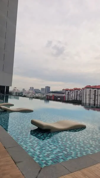 Exterior type: high-rise condominium; features: infinity pool, pool deck with loungers, tiled pool surface with mosaic pattern, surrounding city skyline, modern architectural design, glass railing, manicured landscaping, adjacent residential buildings; style: modern.